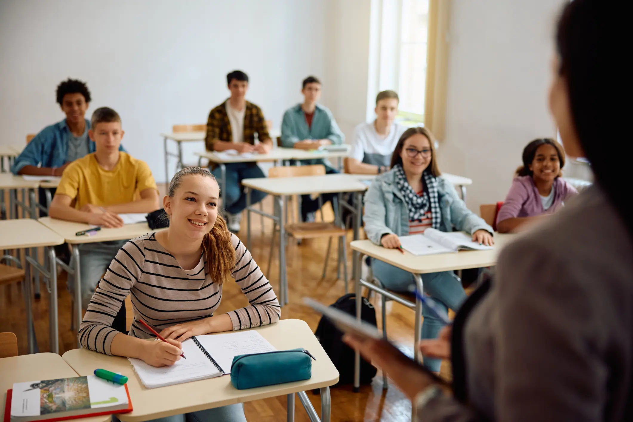 Students attentively listening to a teacher in a bright classroom.