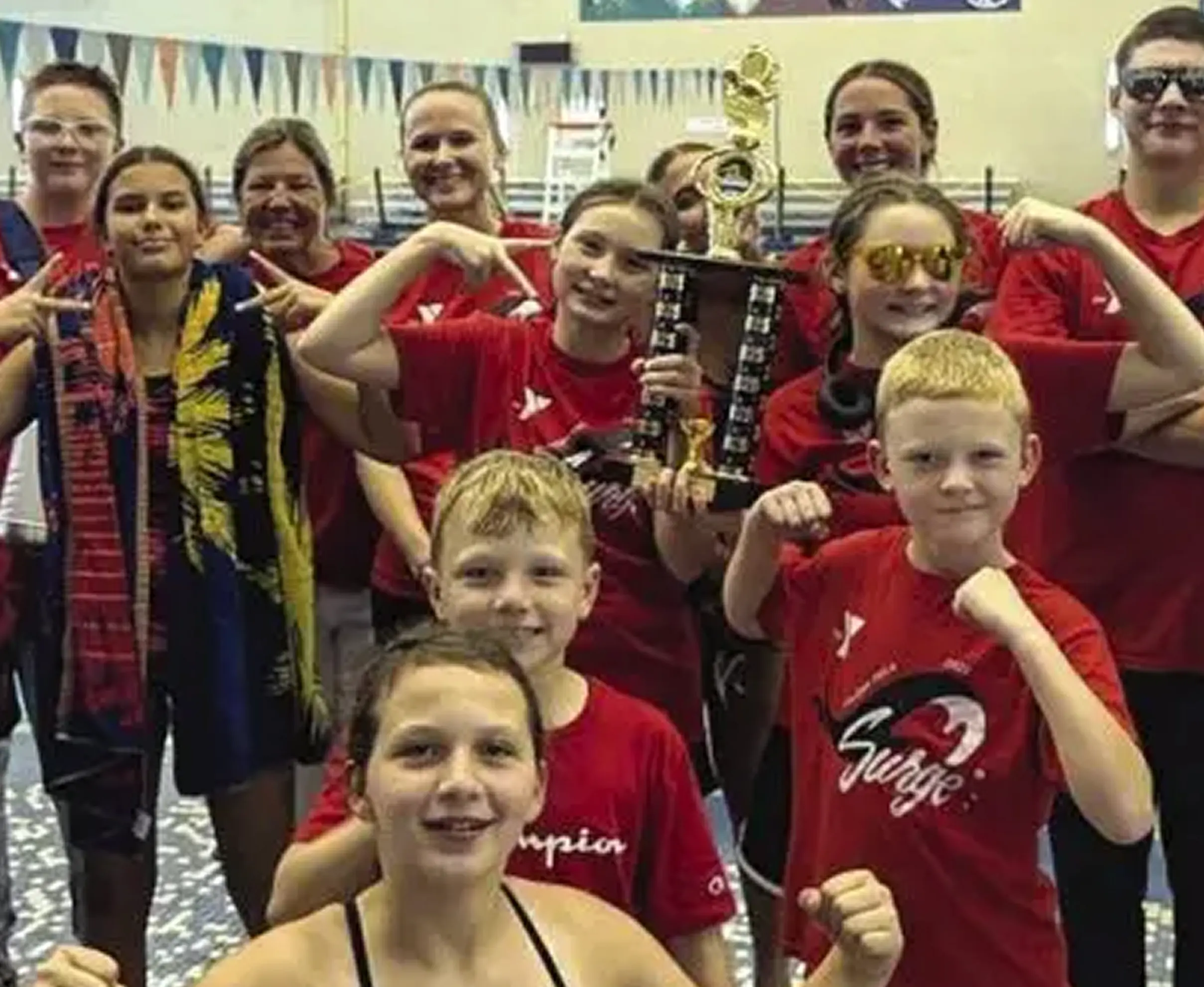 Youth swim team celebrating a victory with a trophy in a pool area.