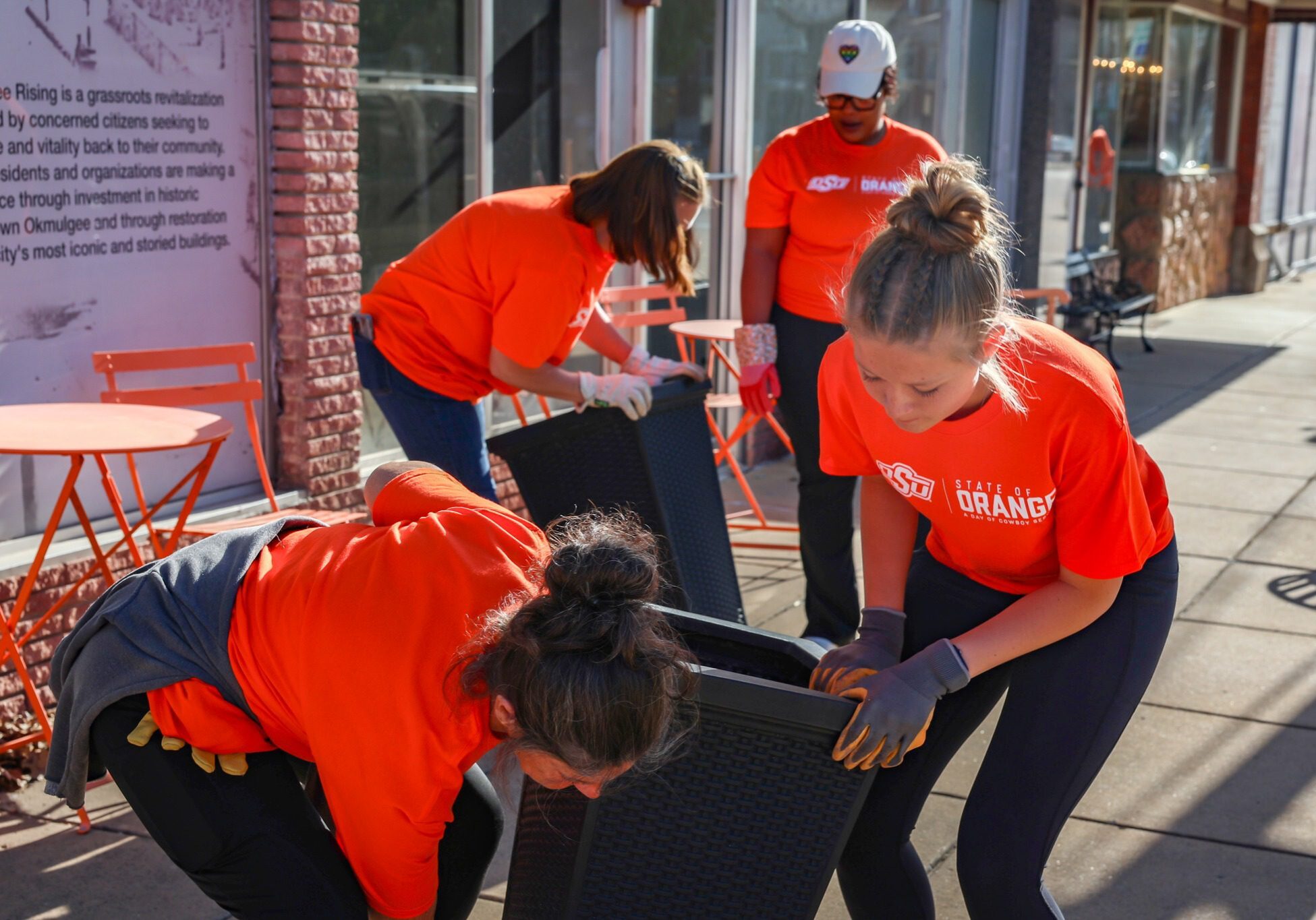 Volunteers in orange shirts assembling furniture outdoors.