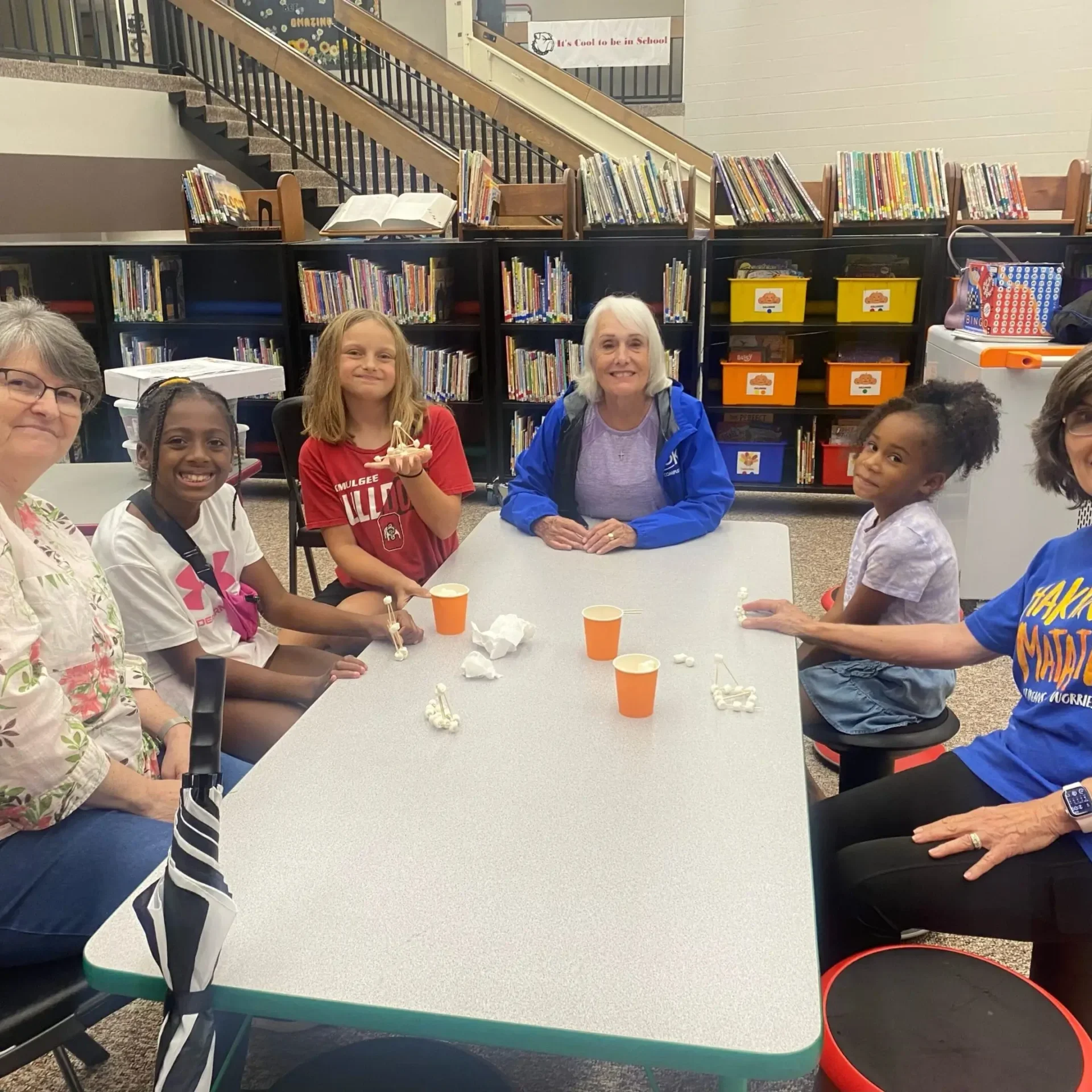 A group of six women sitting around a classroom table, smiling.