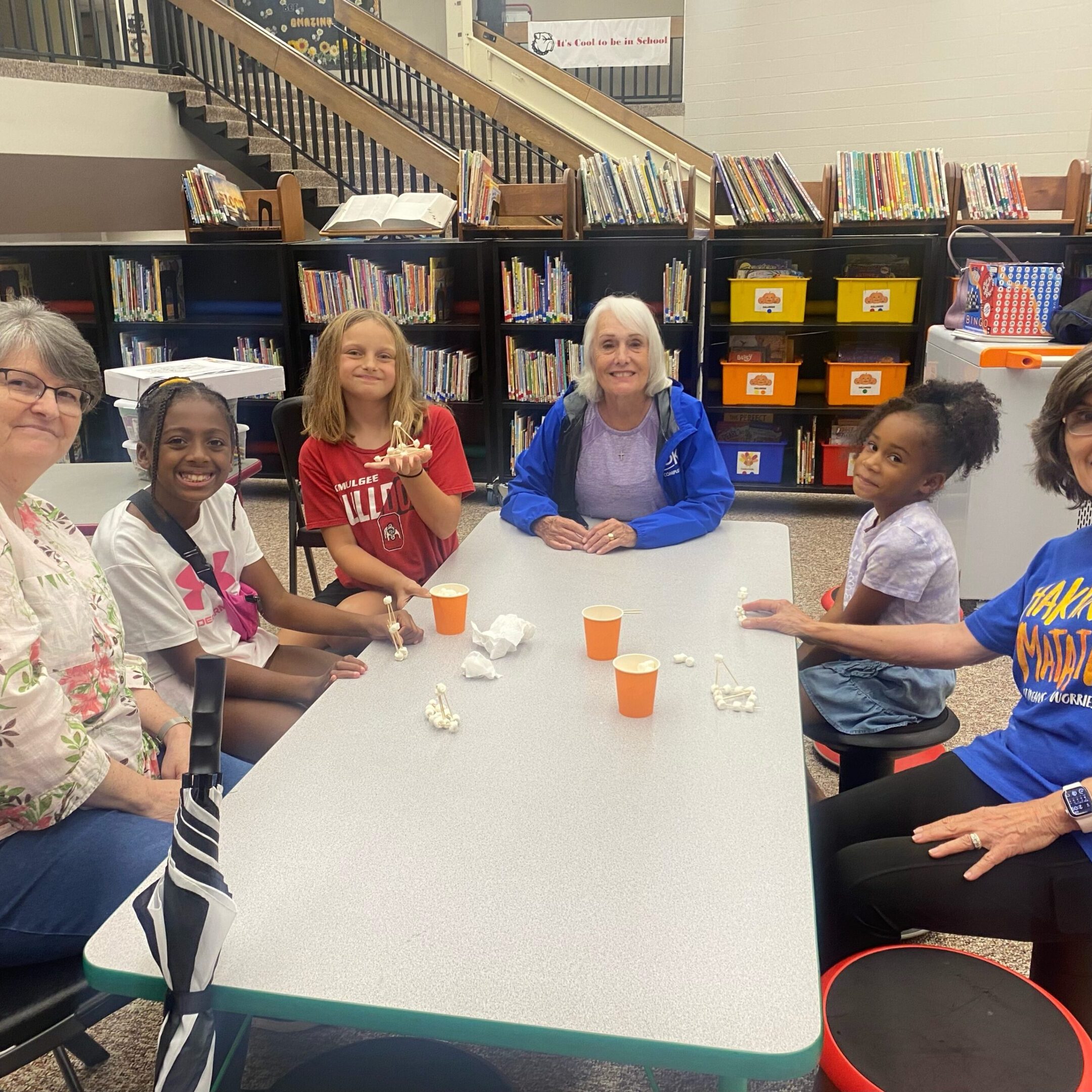 A group of six women sitting around a classroom table, smiling.