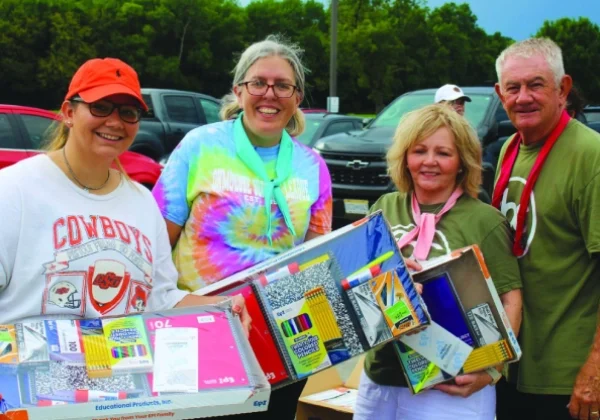 Four smiling adults holding boxes with various items outdoors.